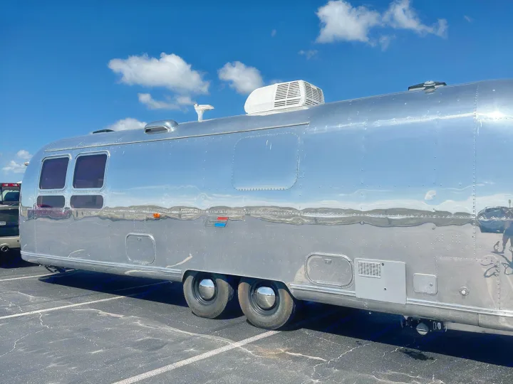 Experience adventure! This polished silver Airstream travel trailer, perfect for RV rental, gleams under a blue sky.. Airstream Sovereign 1973
