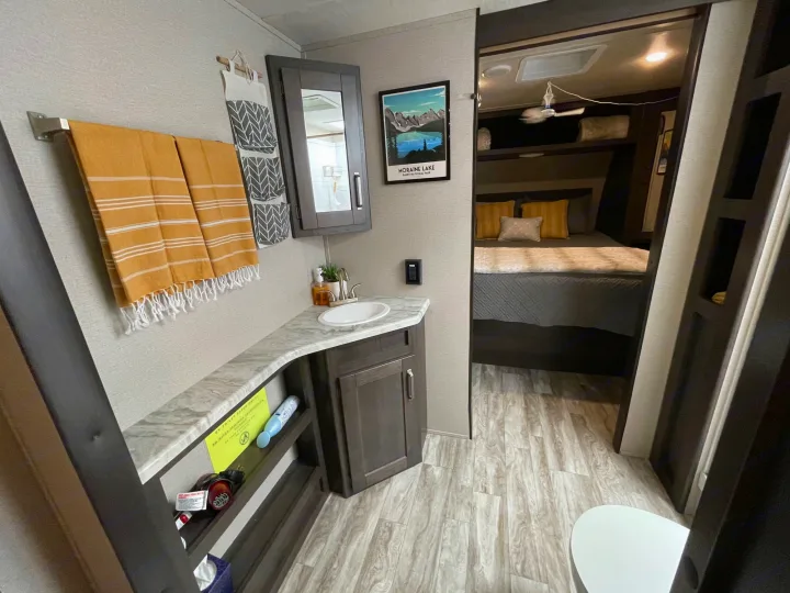 Step inside this RV rental: a practical bathroom vanity with sink, mirror, and storage, leading to a cozy bedroom.. Grand Design Transcend Xplor 2022