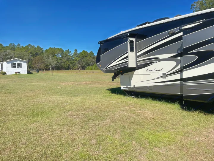 Cardinal Fifth Wheel RV rental parked in a wide grassy field with a house and trees under a clear blue sky, ready for travel.. Forest River Cardinal 2015