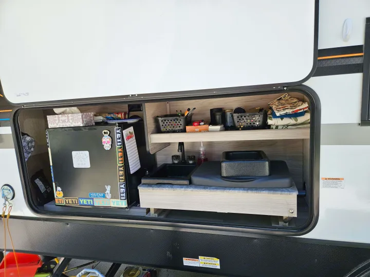 This RV rental's organized outdoor kitchen features a mini-fridge, sink, and covered stovetop for camping.. Coachmen Northern Spirit 2454BH 2022