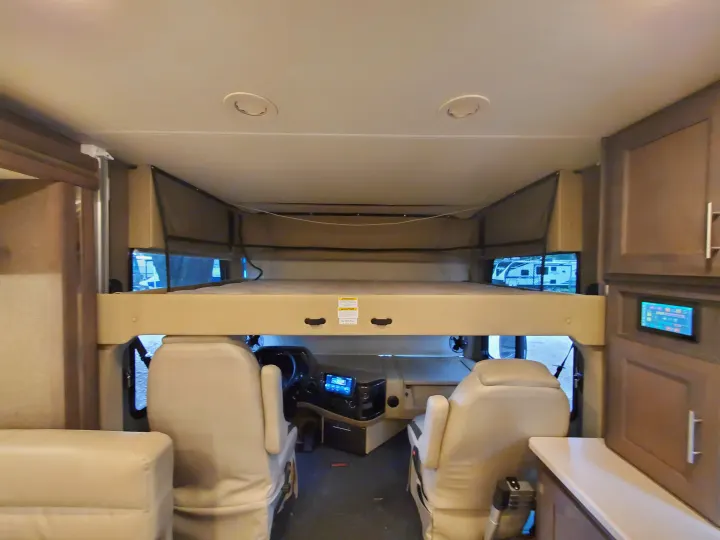 This RV rental interior shows the cockpit seats, overhead bunk bed, and a digital control panel, ready for adventure.. Thor Palazzo 2022