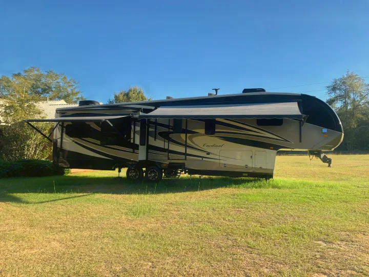 This large fifth-wheel RV, ideal for an RV rental, is set up with awnings extended on a grassy field.. Forest River Cardinal 2015
