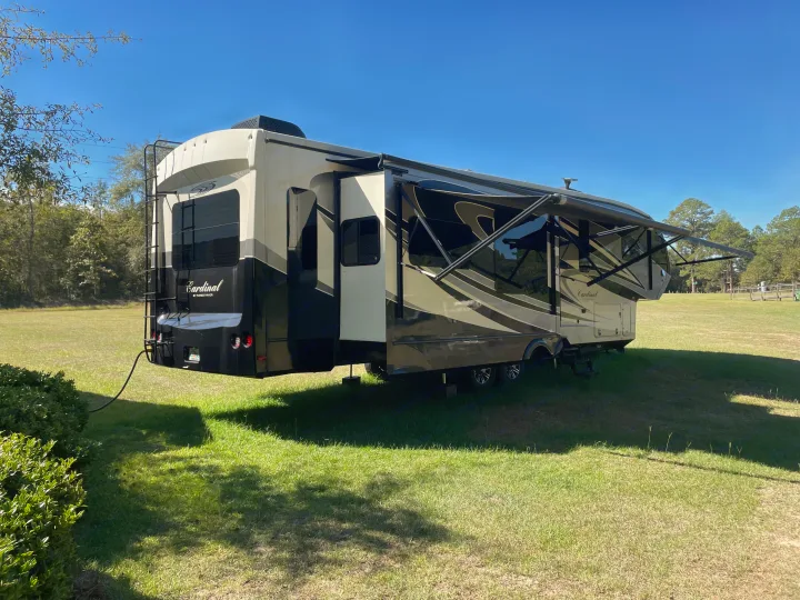 A Cardinal fifth-wheel RV with extended slide-outs and deployed awning in a sunny, grassy field. Great for your next RV rental trip!. Forest River Cardinal 2015