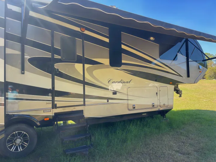 Large Cardinal fifth-wheel RV, cream and black with extended awning, parked on grass. Ideal for an RV rental outdoor trip.. Forest River Cardinal 2015