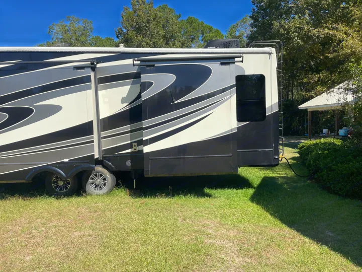 A large fifth-wheel RV rental, black, white, and grey, parked on a green campsite under a clear sky. Features visible slide-outs and a ladder.. Forest River Cardinal 2015