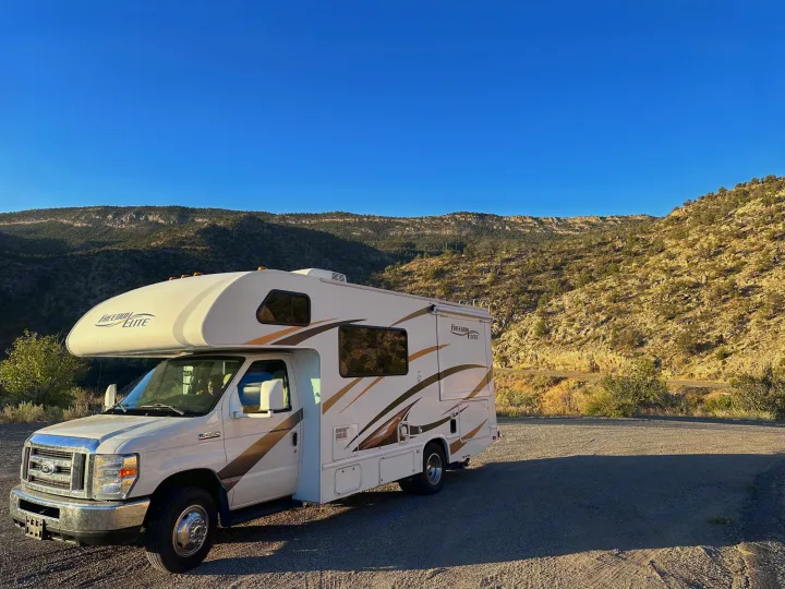 White Freedom Elite RV rental parked on a gravel lot, with arid mountains and a clear blue sky in the background.. Thor Freedom Elite 2016