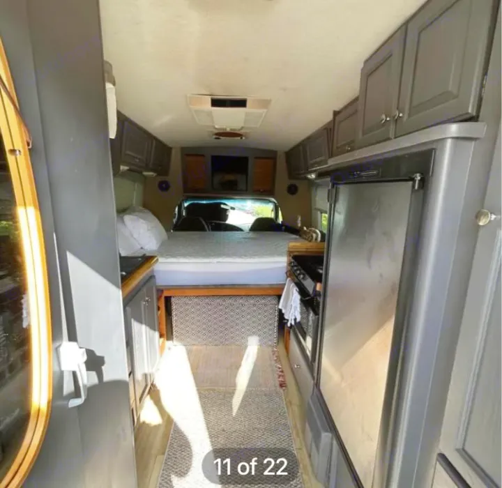 RV rental interior: Looking down the aisle to a bed. Kitchen appliances (fridge, stove) and gray cabinets line the space.. Ford Econoline 2004