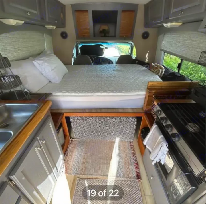 Spacious RV rental interior. Features a cozy bed over the cab, sink, and gas range. Compact travel comfort.. Ford Econoline 2004