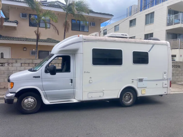 White Ford E-350 B-Plus RV rental, a camper van, parked on a street in front of buildings.. Ford Econoline 2004