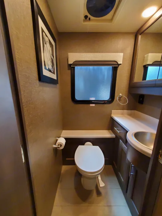 This rv rental bathroom features a compact toilet, sink, mirror, and window, optimizing space for travel comfort.. Thor Palazzo 2022