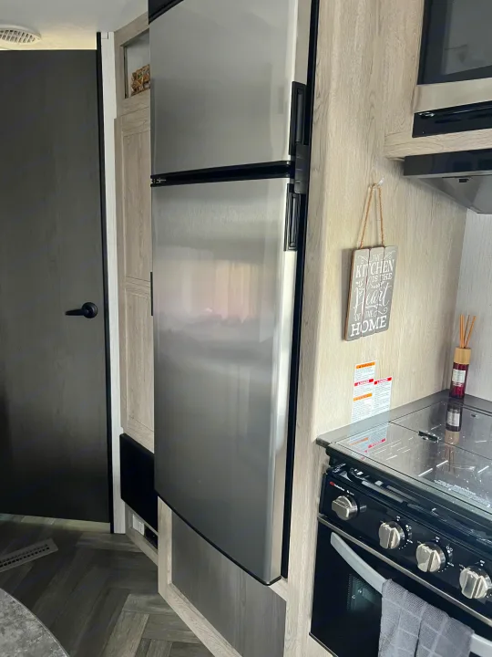 Inside a modern RV rental: stainless steel fridge, stove, and microwave in a sleek grey kitchen.. Keystone Prowler 2021