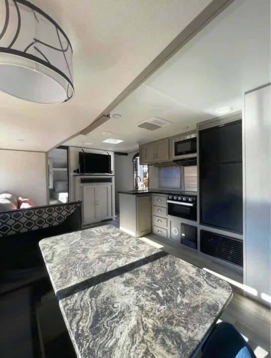 Inside a clean RV rental: kitchen with stove/fridge, dining booth, TV area, and cozy bunk beds visible.. Forest River Tracer 2021