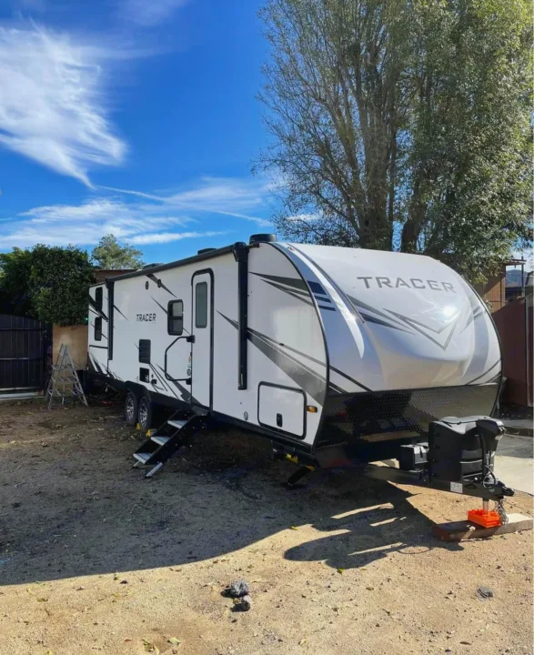 New white Tracer travel trailer with steps, ideal for RV rental. Parked outside under a clear blue sky.. Forest River Tracer 2021