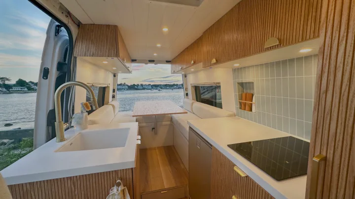 Modern camper van interior with fluted wood kitchen, cozy dining area, and stunning water view, ideal for an RV rental.. Mercedes-Benz Sprinter 2020