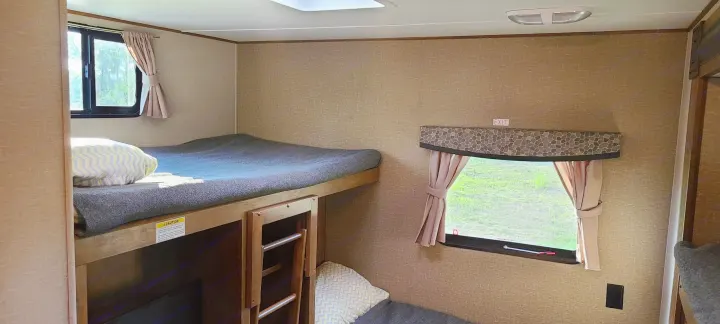 Cozy bunk beds in an RV rental, featuring light-filled windows with outdoor views. A functional sleeping space for trips.. Crossroads RV Z-1 2016