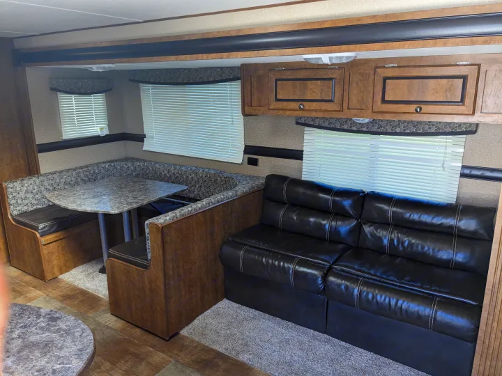 Inside an RV rental: a cozy living area with a U-shaped dinette and a black leather sofa, ideal for travel.. Crossroads RV Z-1 2016