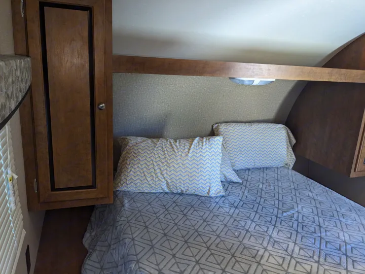Cozy RV rental bedroom with patterned pillows on a comfortable bed and wooden cabinetry, perfect for a compact interior.. Crossroads RV Z-1 2016