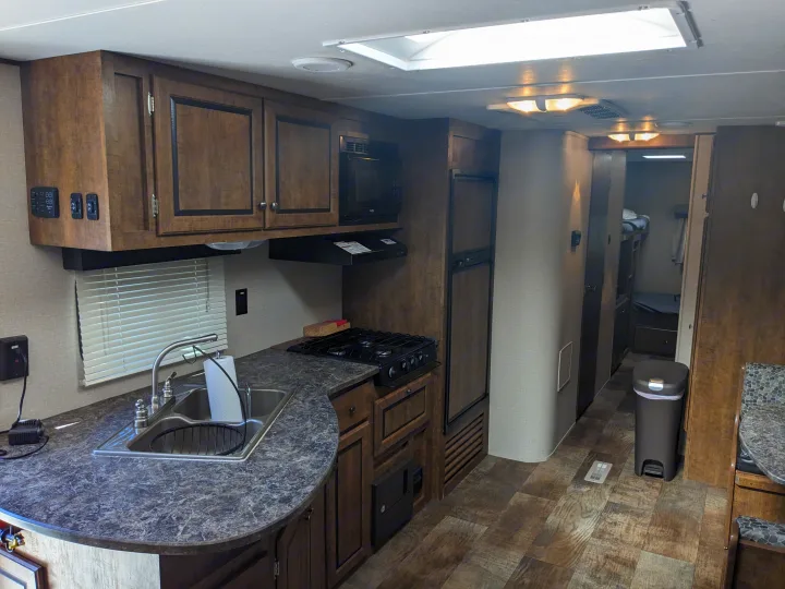 Compact RV rental kitchen: sink, stove, microwave, and fridge. Bunk beds in back. This functional space offers comfort for your travels.. Crossroads RV Z-1 2016