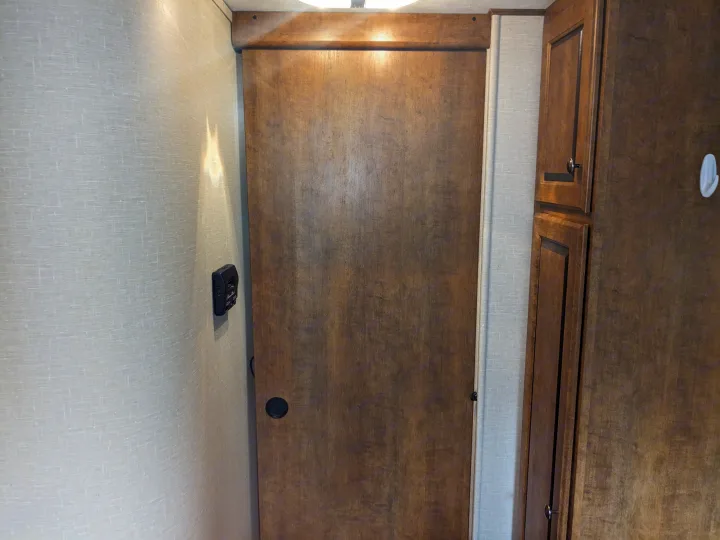 RV rental interior featuring a light-colored textured wall with a control panel, and a dark wooden sliding door next to a brown cabinet.. Crossroads RV Z-1 2016