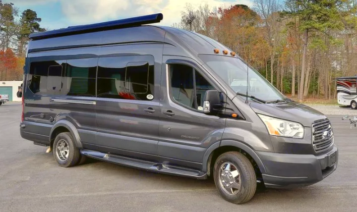 This gray Ford Transit van is converted into an RV rental, featuring an awning, custom windows, and side steps.. Coachmen CrossFit 22c 2019