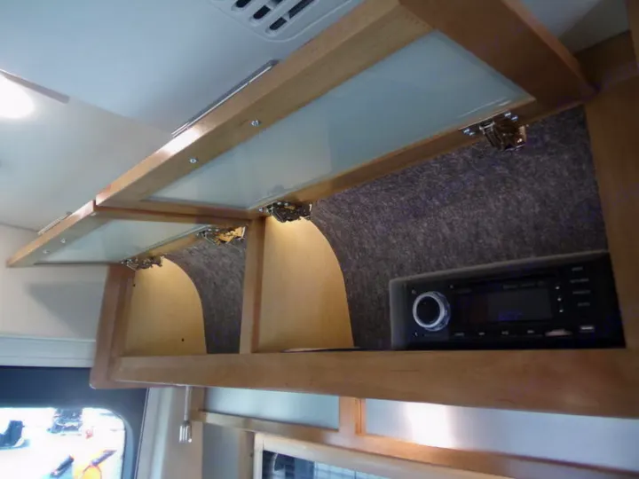 RV rental overhead cabinets with an integrated stereo system. Features light wood, opaque glass doors, & felt-lined storage.. Coachmen CrossFit 22c 2019