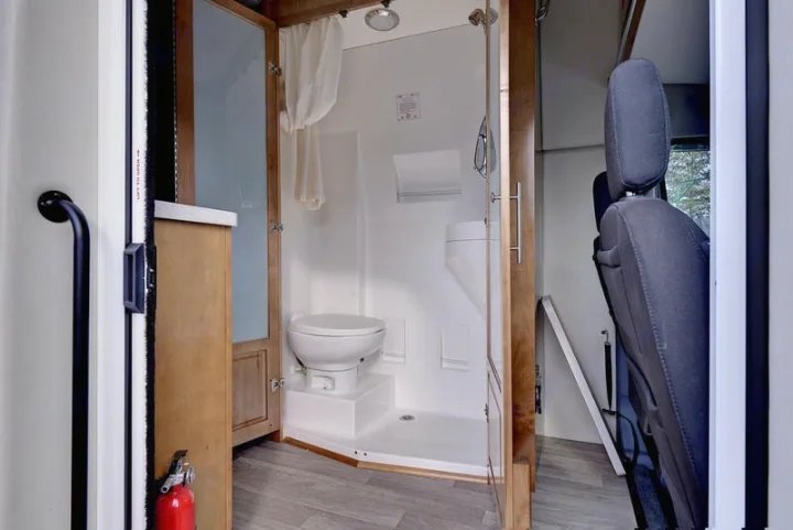 Compact RV rental bathroom with toilet, shower, and safety features like a grab handle and fire extinguisher.. Coachmen CrossFit 22c 2019