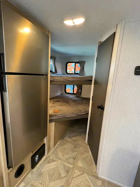 RV rental interior featuring a stainless steel fridge, two bunk beds with windows, and light patterned flooring.. Forest River Salem Cruise Lite 2024