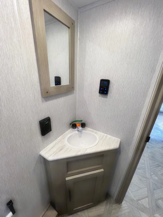 Explore this RV rental's compact bathroom, featuring a corner sink, mirror, and modern digital controls on textured walls.. Forest River Salem Cruise Lite 2024