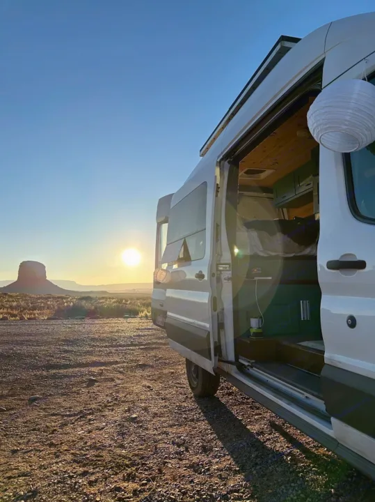 This RV rental offers sunset views over a desert mesa. Its open side door reveals a cozy, wood-paneled interior.. Ford Transit 2017