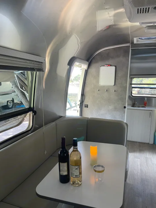 Cozy RV rental interior with wine, perfect for a relaxing getaway. Dinette, kitchen, and bright windows.. Airstream Bambi 2020