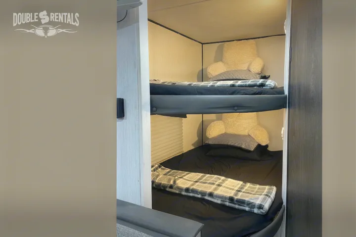 Inside an RV rental: two well-made bunk beds with black sheets, plaid blankets, and cozy backrest pillows.. Heartland Trail Runner 2021