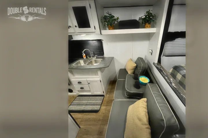 Cozy **RV rental** interior: shows a compact kitchen with sink, dinette seating with cup holders & popcorn, plus a bed area.. Heartland Trail Runner 2021
