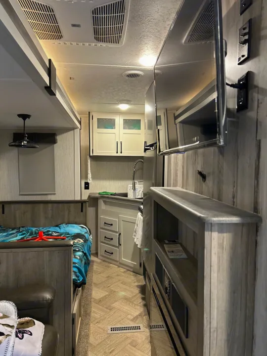 RV rental: Compact interior showing kitchenette, sleeping area with bed, and mounted TV with shelves.. Puma Palomino 2021