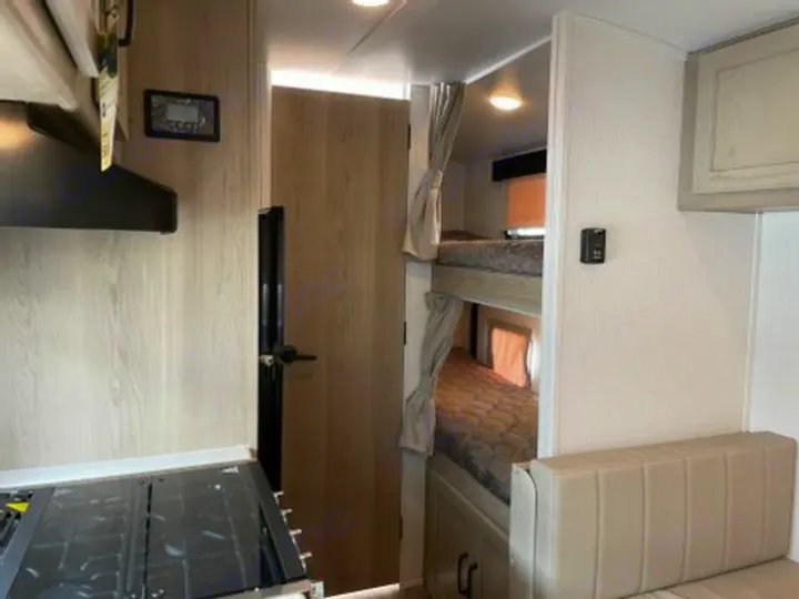Inside an RV rental, showing a modern kitchen, cozy bunk beds with curtains, and a comfortable dinette seating area.. Forest River Rockwood Geo Pro 2022