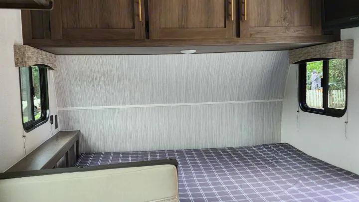 RV rental bedroom with a comfy bed, wooden overhead cabinets, and a side bench. Large windows offer outdoor views.. Forest River Viking Ultra Lite 2022