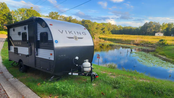 Viking travel trailer, ideal for an RV rental, parked roadside by a tranquil pond with lily pads.. Forest River Viking Ultra Lite 2022