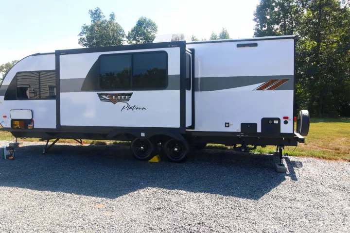 Modern white RV, an ideal rv rental, with slide-out extended on a gravel lot.. Forest River Wildwood X-LITE 240BHXL 2024