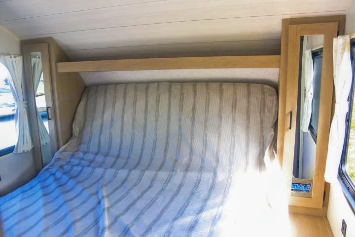 RV rental interior: a cozy bedroom with a striped bed, built-in storage, and windows.. Forest River Wildwood X-LITE 240BHXL 2024