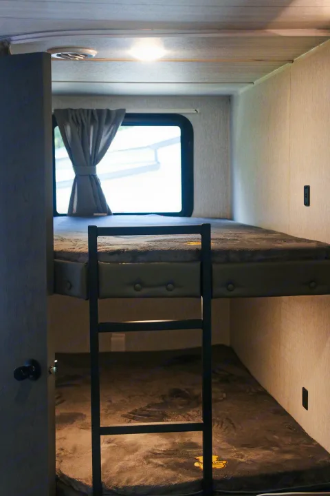 RV rental interior: two cozy bunk beds with ladder, window, and plush grey bedding. Ideal for family trips.. Forest River Wildwood X-LITE 240BHXL 2024