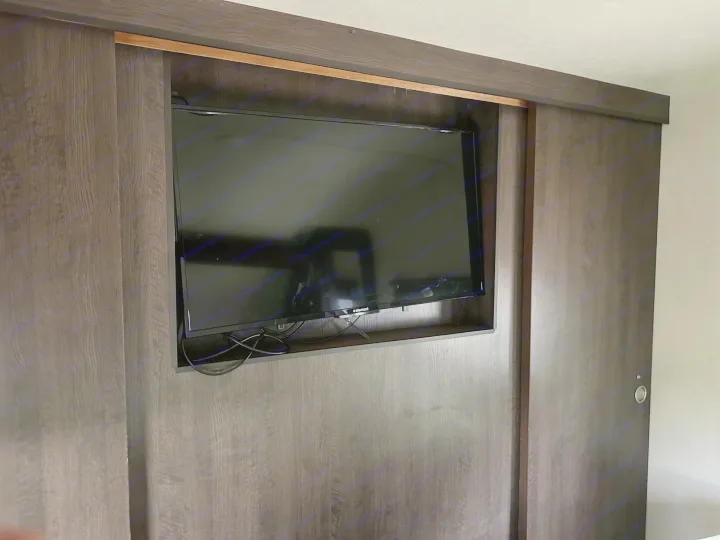 An rv rental features a dark wood built-in TV cabinet with sliding doors. Cables are visible beneath the screen.. Forest River Wildwood X-Lite 2018