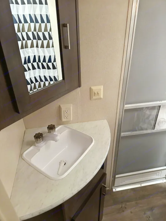 Compact RV rental bathroom. Features a vanity with a sink, faucet, mirror, outlets, and a shower.. Forest River Wildwood X-Lite 2018