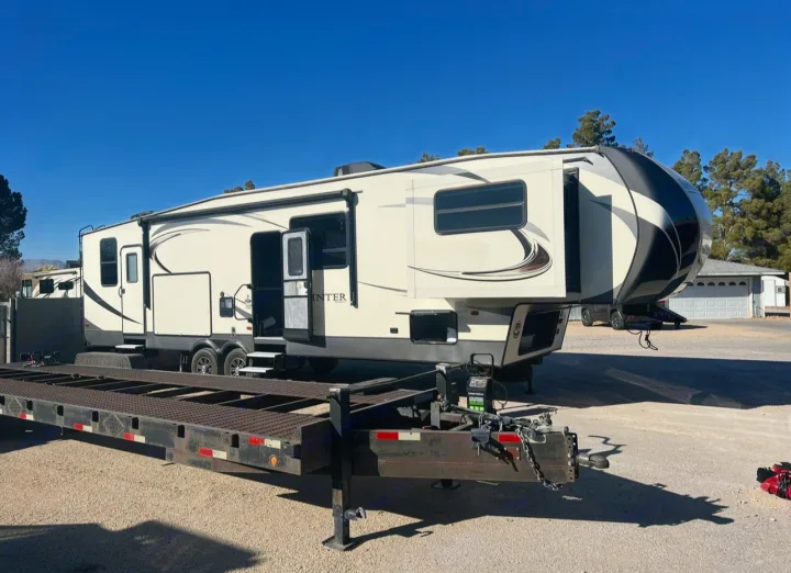 A cream-colored Sprinter fifth-wheel rv rental is parked on a gravel lot with slide-outs extended and doors open.. Keystone RV Sprinter 2018