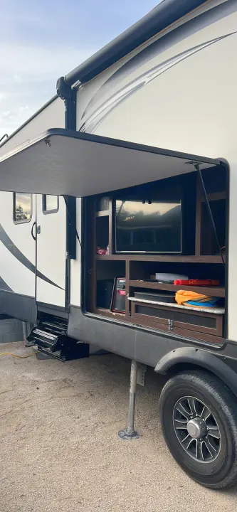 Explore this RV rental's side compartment featuring an outdoor TV, shelves, and extended steps.. Keystone RV Sprinter 2018