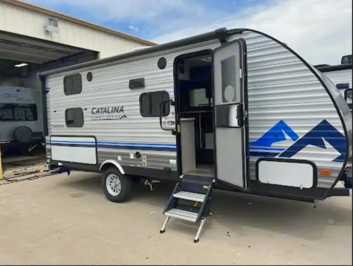Ready for adventure! This gray and blue Catalina Summit Design travel trailer RV rental, with open door and steps, awaits.. Coachmen Catalina Summit 2022
