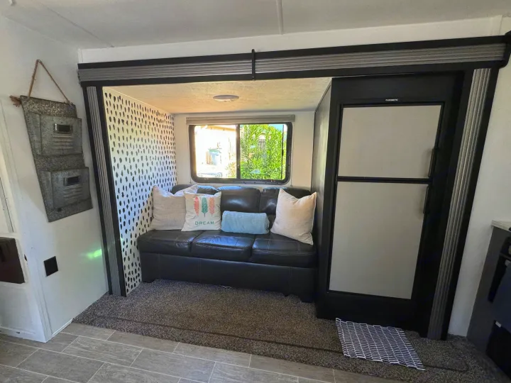 Spacious rv rental interior: black sofa in slide-out, window view, and built-in refrigerator.. Heartland RVs Trail Runner 2020