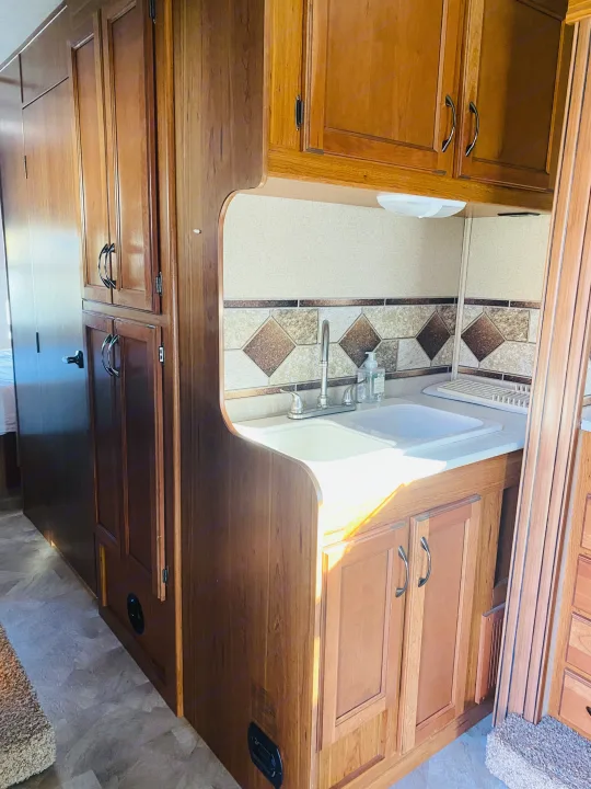Interior of an RV rental showing a well-lit kitchen area with wood cabinets, a sink, and a tiled backsplash.. Jayco Redhawk 2016