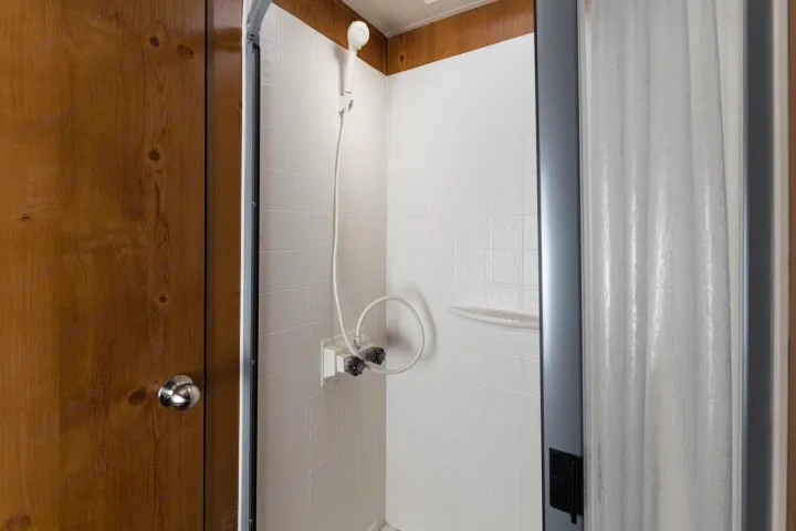 Inside a compact RV rental, this shower features a handheld sprayer, white tile-patterned walls, and simple controls.. Gulf Stream Cruiser 2021