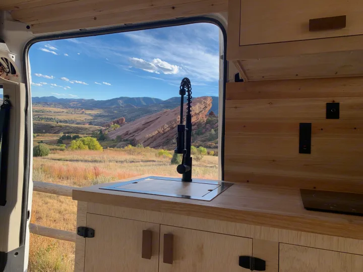 RV rental kitchen setup with a stunning view of red rock mountains and a vast landscape through the open van doors.. RAM Promaster 2500 159wb 2018