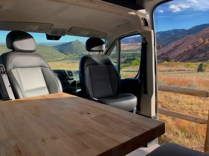 RV rental camper van interior: wooden table, front seats, and scenic views of mountains, fields, and red rock formations.. RAM Promaster 2500 159wb 2018