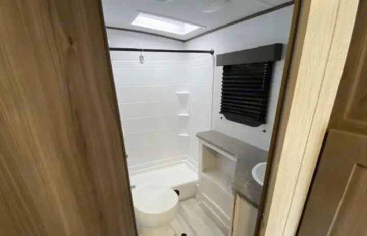Inside an RV rental: a modern, compact bathroom with white shower, toilet, vanity, and a ceiling skylight.. Cruiser RV MPG 2023